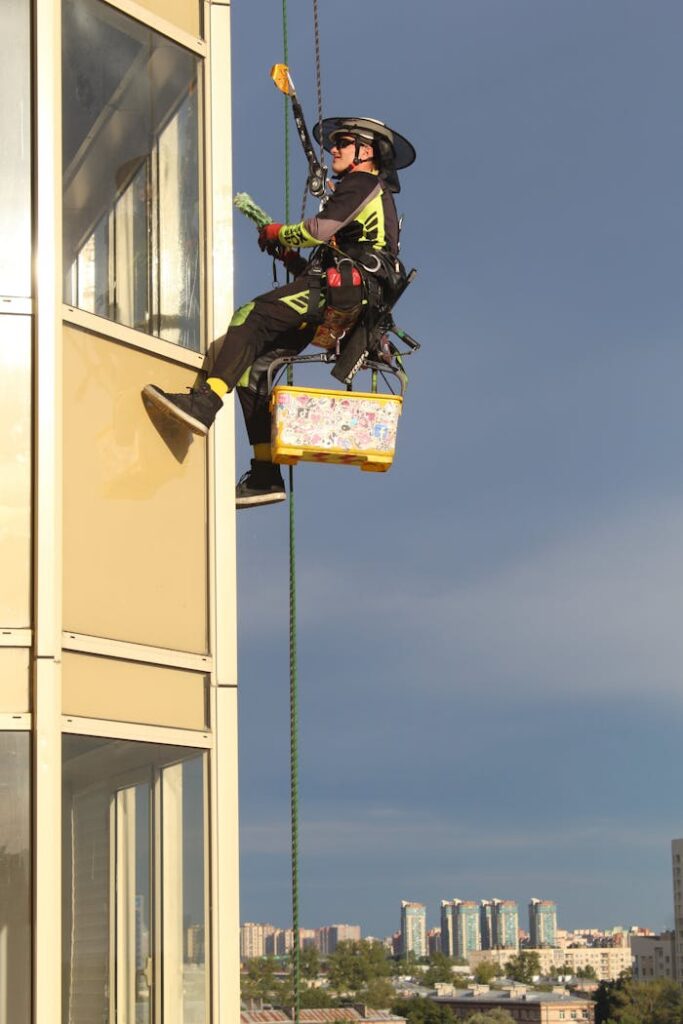 A professional window cleaner suspended by ropes on a high-rise building, with a cityscape background.