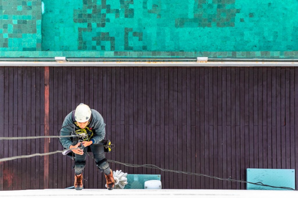 A worker using safety equipment for exterior building maintenance, viewed from above.
