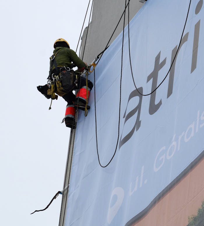 Worker using rope access for installing a large outdoor banner on a building.