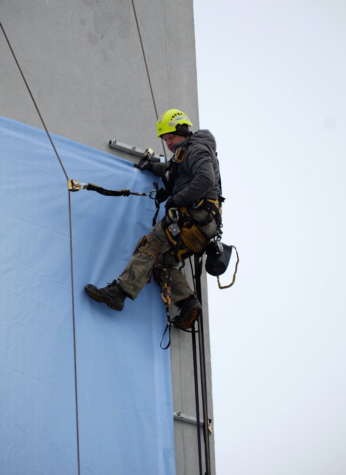 Rope access technician expertly fixing large poster on high-rise building.